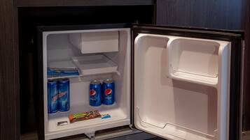 A refrigerator with two shelves, one containing two cans of Perrier and two cans of Pepsi, and the other shelf holding a chocolate bar and a box of tissues.