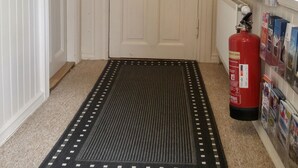 A hallway with a white door, a black and white patterned rug, a fire extinguisher, and a shelf with magazines. - Guesthouse Sólgarðar (Akureyri)