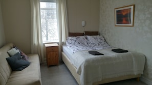 A bedroom with a bed, a bedside table, a nightstand, a window with curtains, a wall-mounted lamp, and a framed picture. - Guesthouse Sólgarðar (Akureyri)