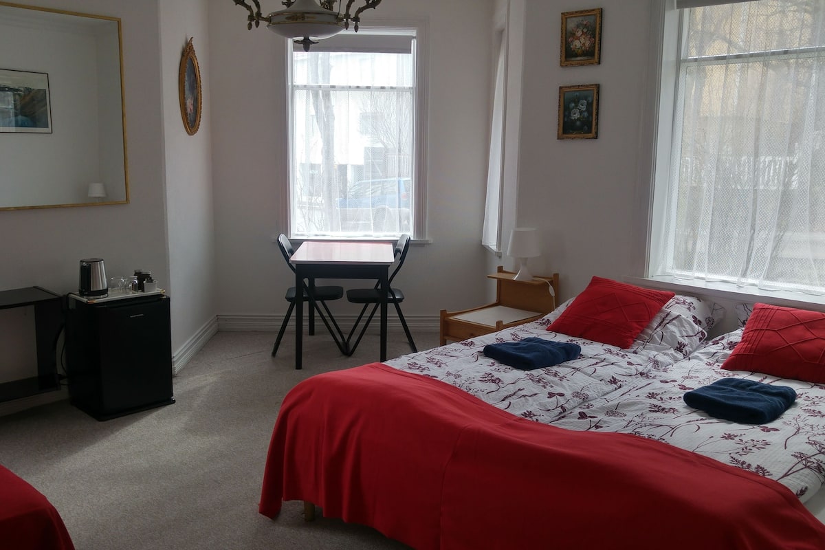 A bedroom with a bed, a desk, and a chair. There is a window with a view of the outside.