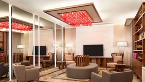 Un hall d’hôtel moderne doté d’un grand miroir, de sièges confortables, d’un téléviseur à écran plat et d’un luminaire décoratif rouge.