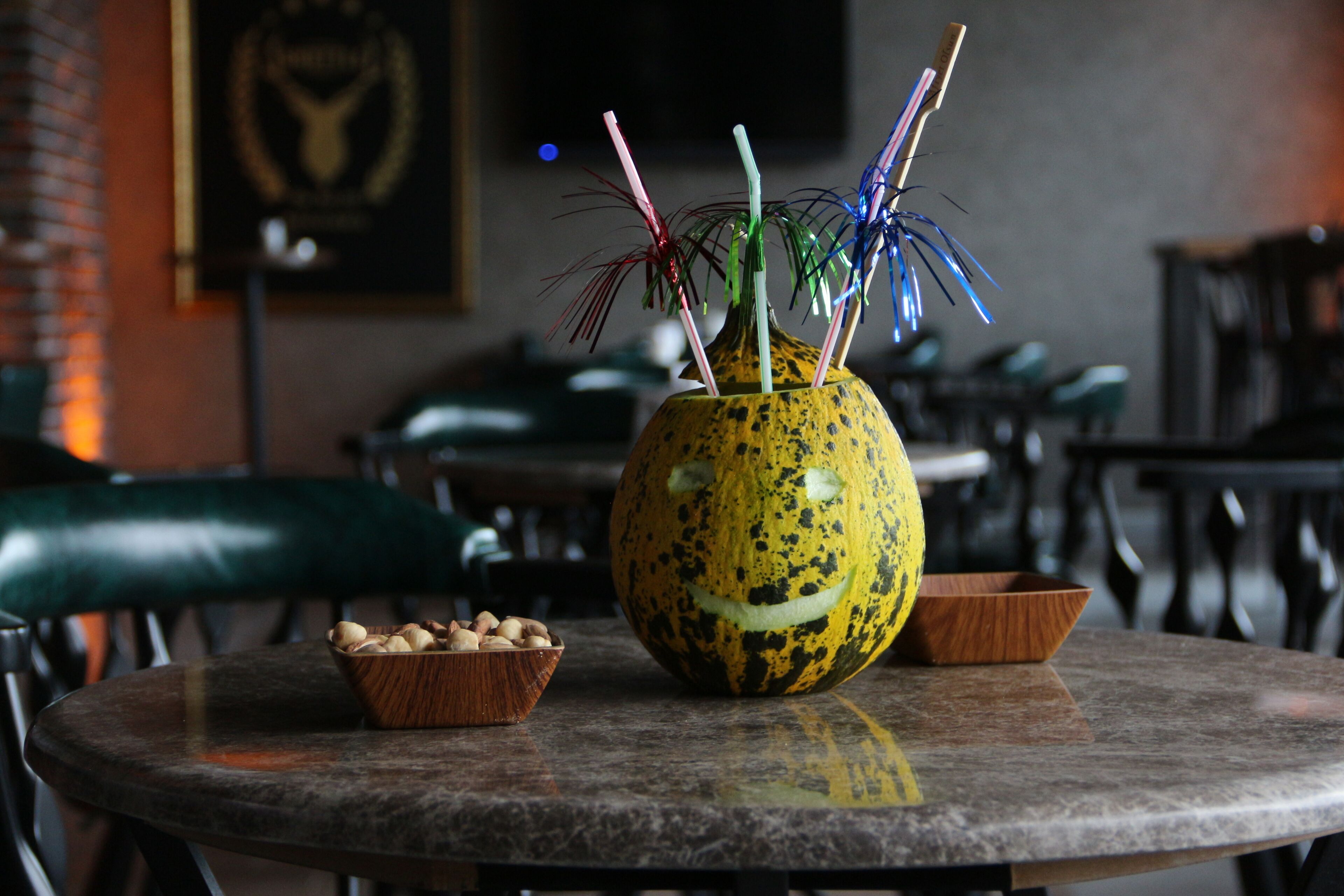 A round table with a carved pumpkin centerpiece, a small bowl of nuts, and a wooden bowl.