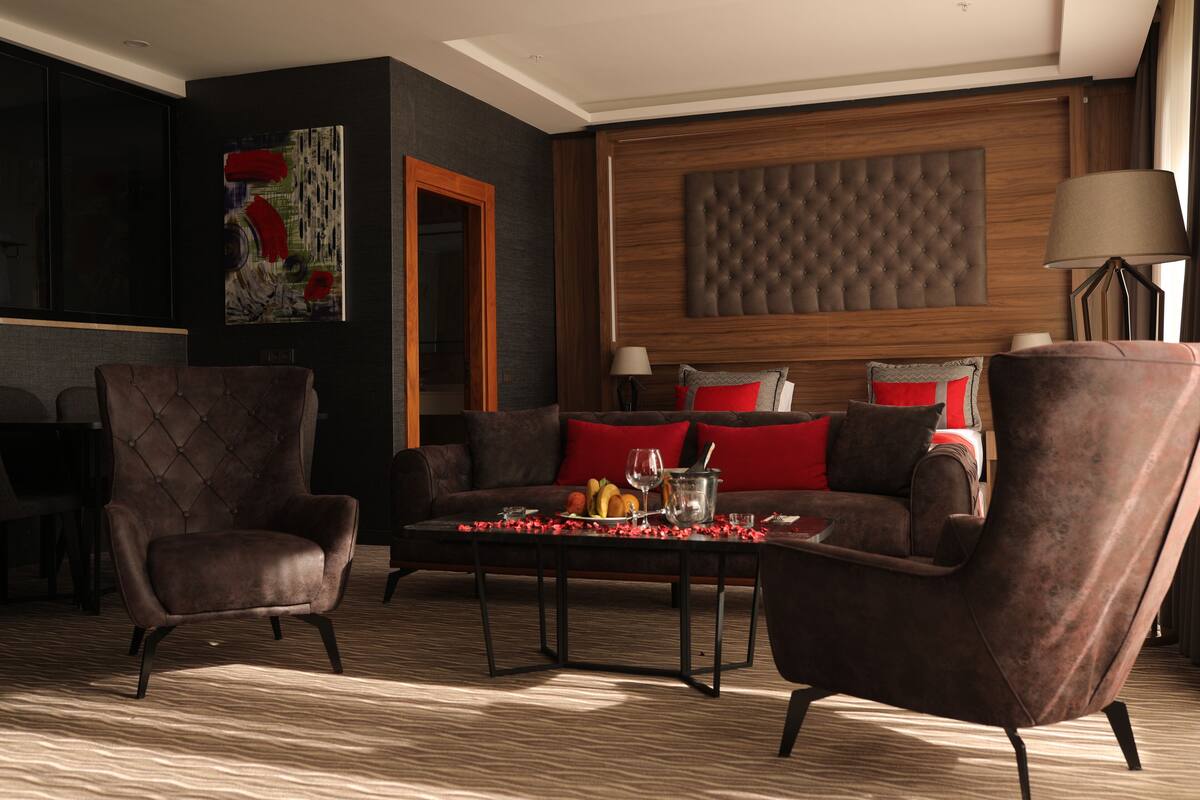 Una habitación de hotel moderna con cabecera de madera oscura, un sofá tapizado y una zona de comedor con una mesa dispuesta para dos personas.