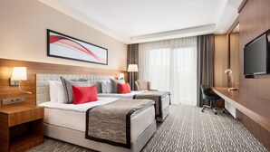 Une chambre d’hôtel avec deux lits, un bureau, une télévision et une grande fenêtre avec des rideaux.