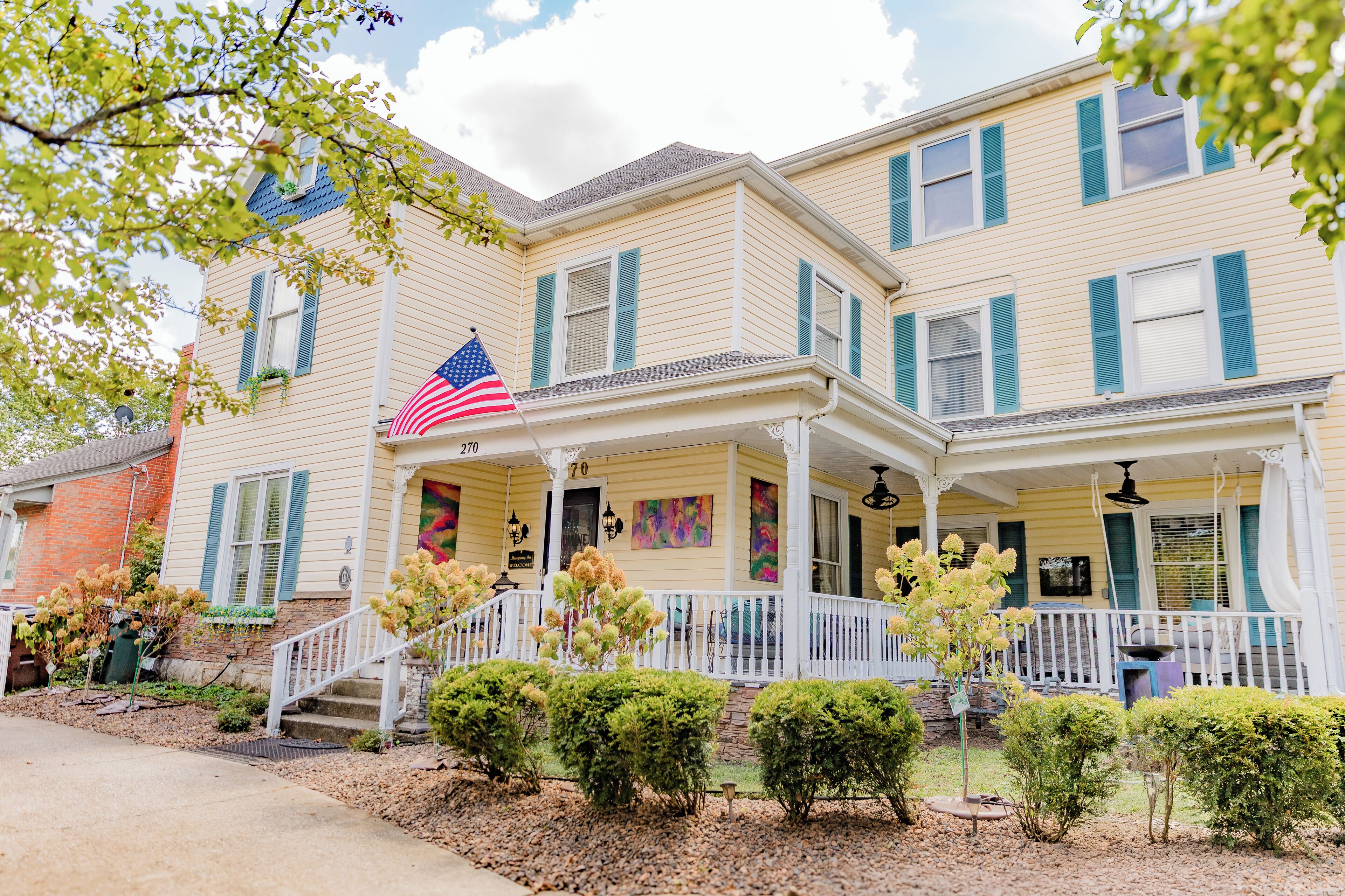 A two-story house with a porch, a small garden, and an American flag.