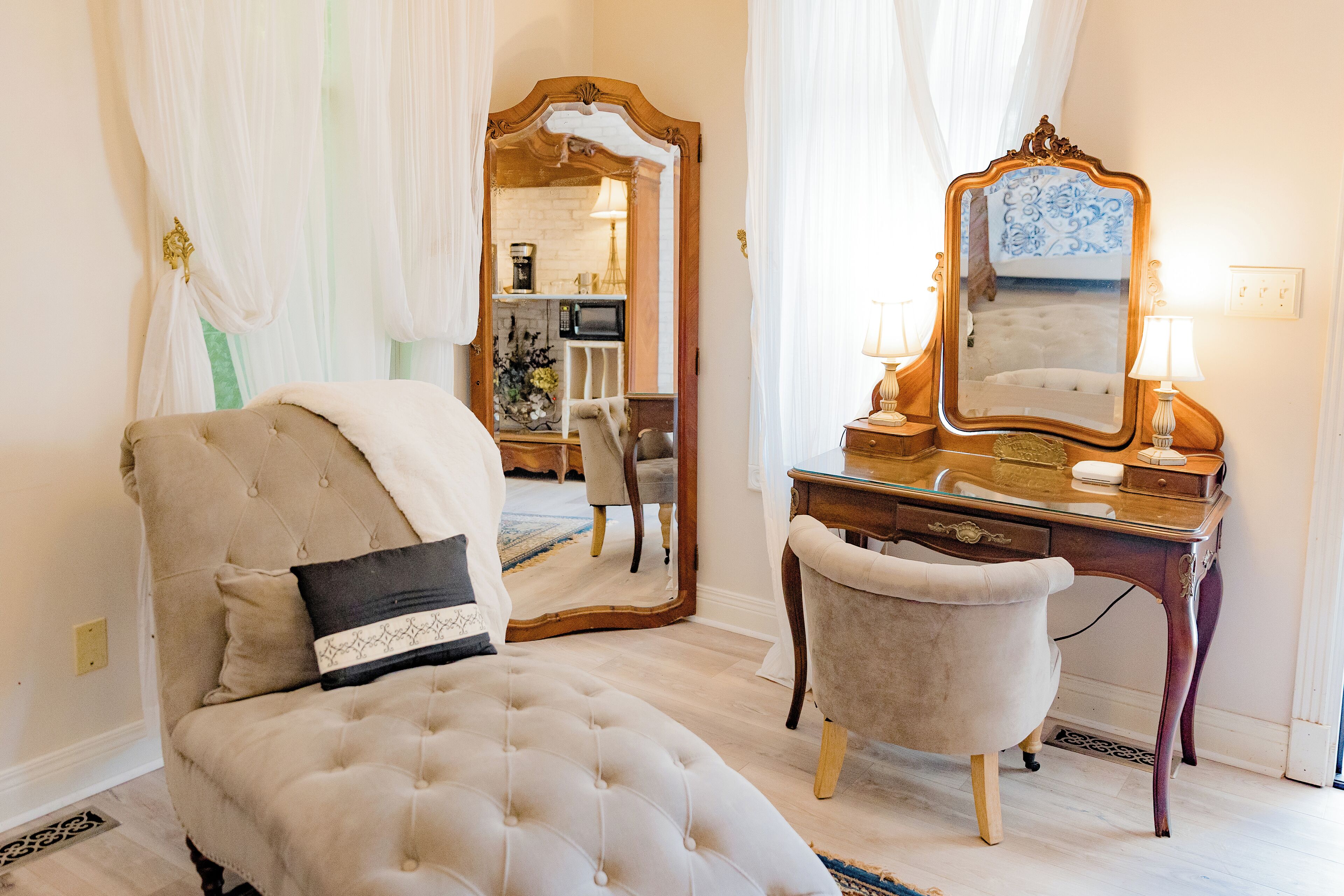 A bedroom with a tufted bed, a vanity with a mirror, and a chair.