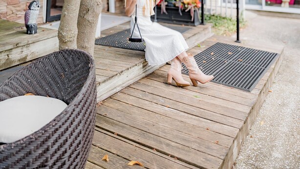 A woman sitting on a wicker chair under a tree, with a building labeled "hello" in the background. - Montgomery Inn BnB (Versailles)