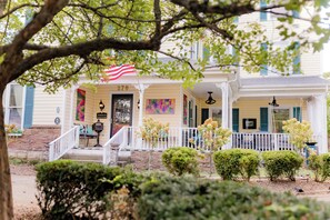 A two-story house with a porch, a small garden, and an American flag.
