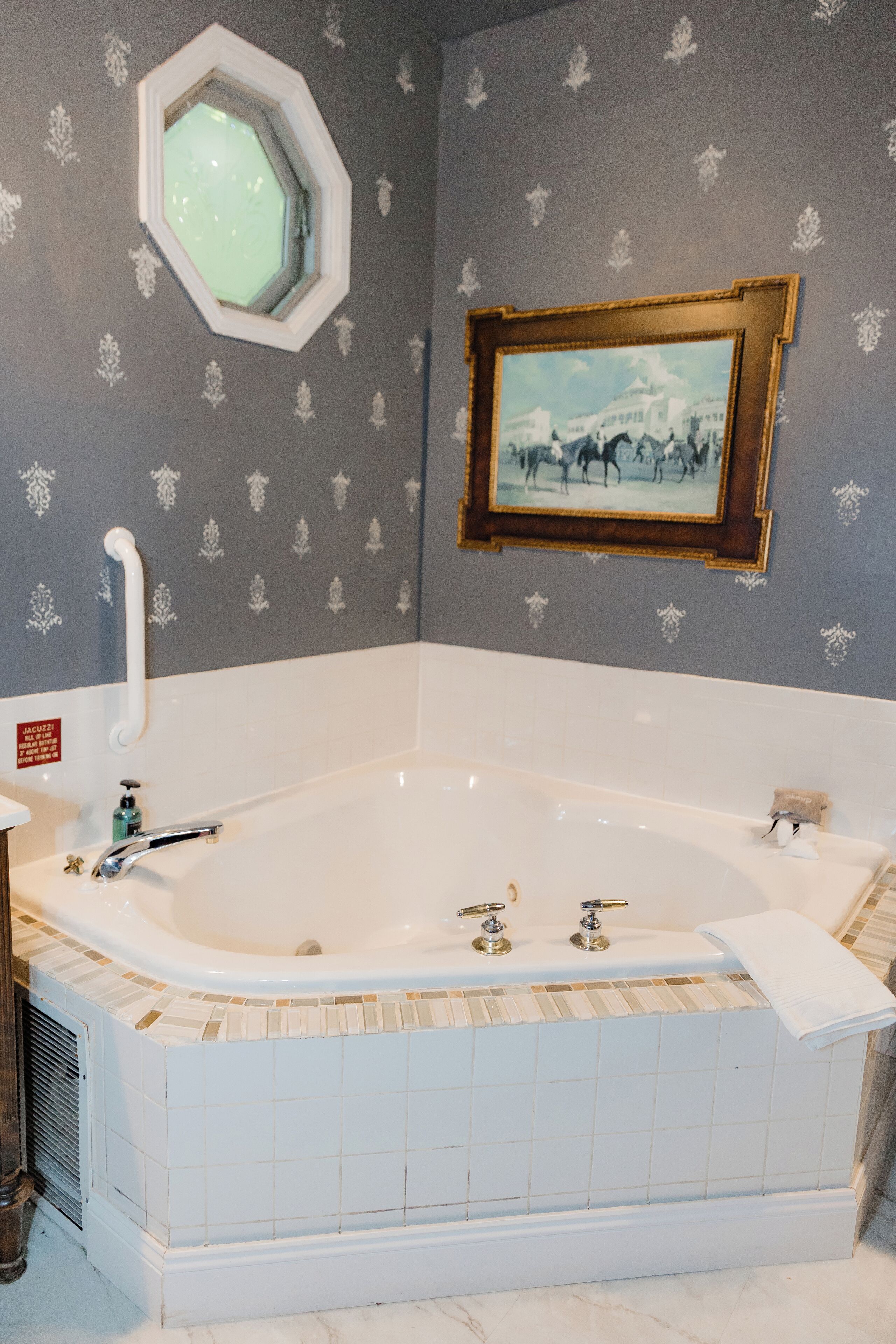 A bathroom with a large bathtub, a window, and a framed picture on the wall.