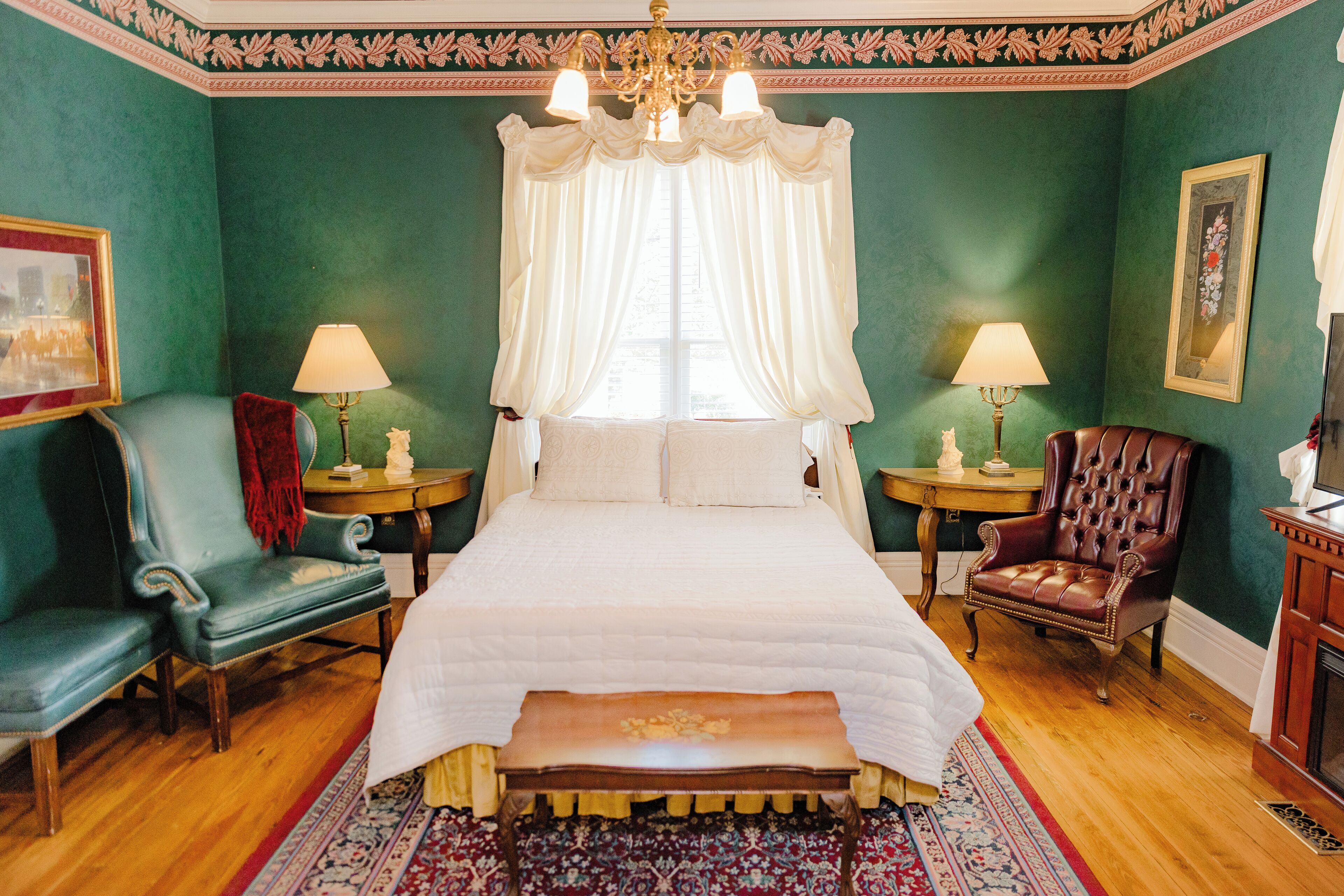 Une chambre à coucher avec un grand lit, deux tables de chevet, une chaise, un banc et un lustre.
