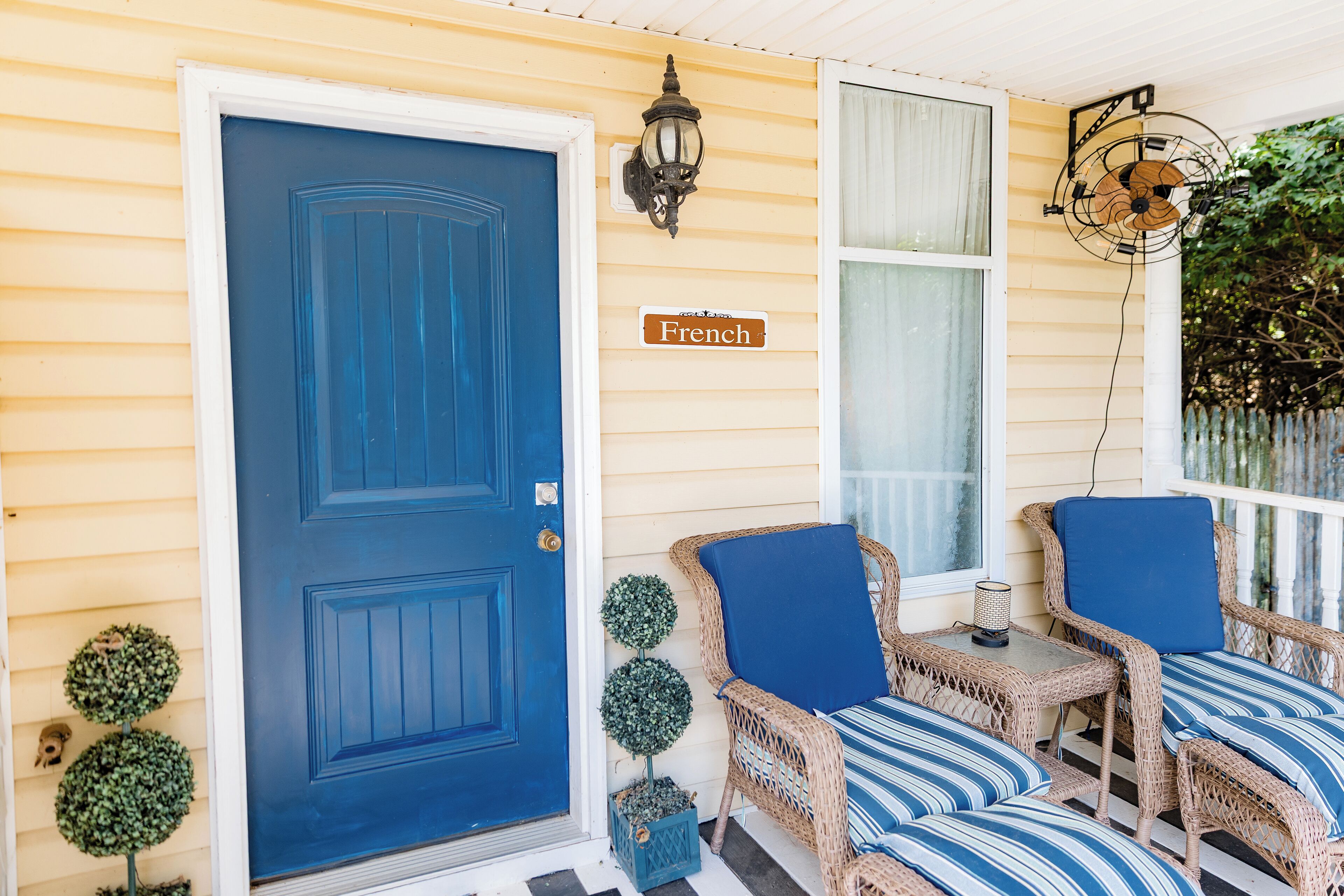 A porch with a blue door, wicker chairs with blue cushions, and a sign that reads "French".