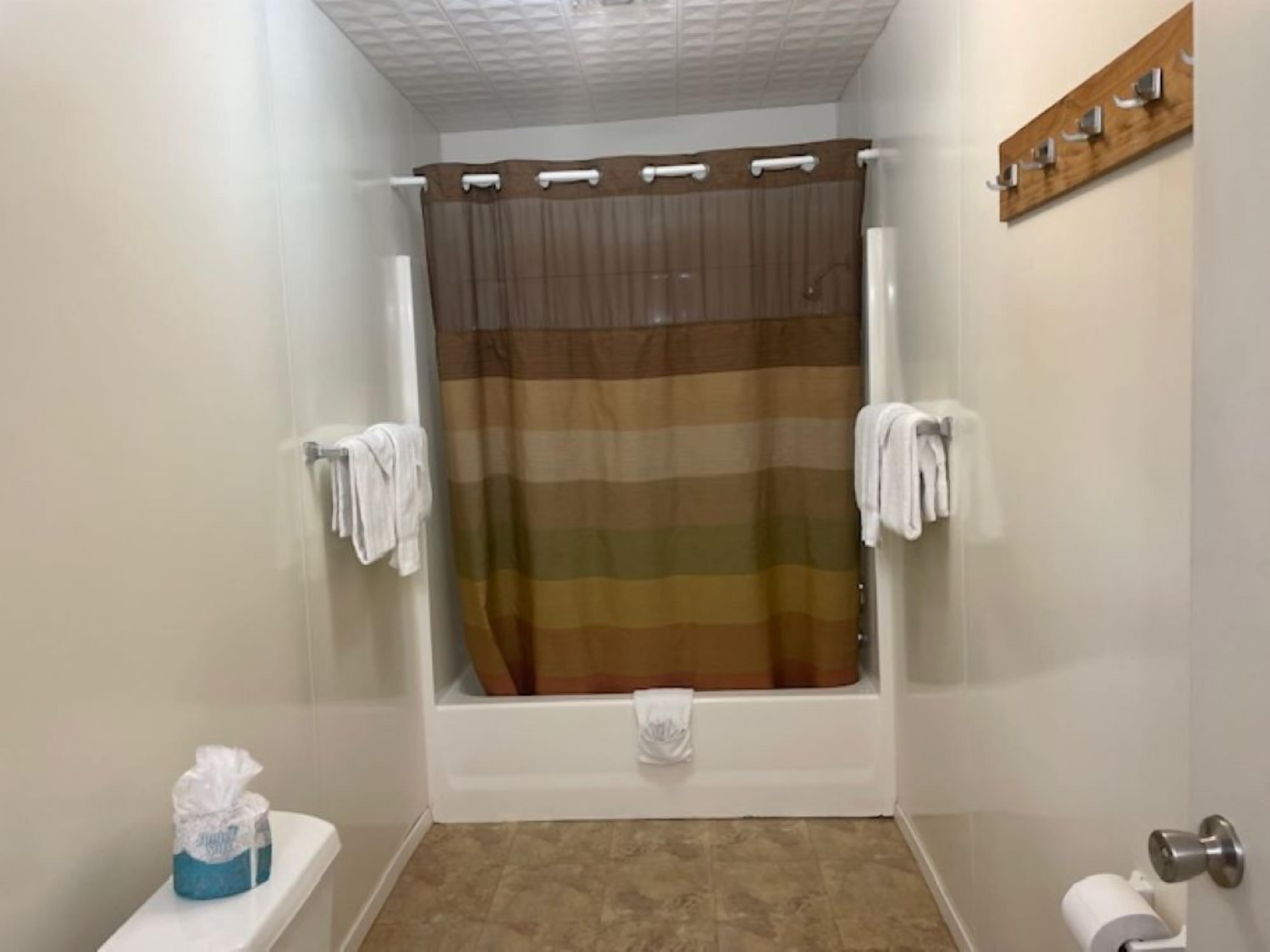 Un baño con cortina de ducha, inodoro, toallero y dispensador de papel higiénico.