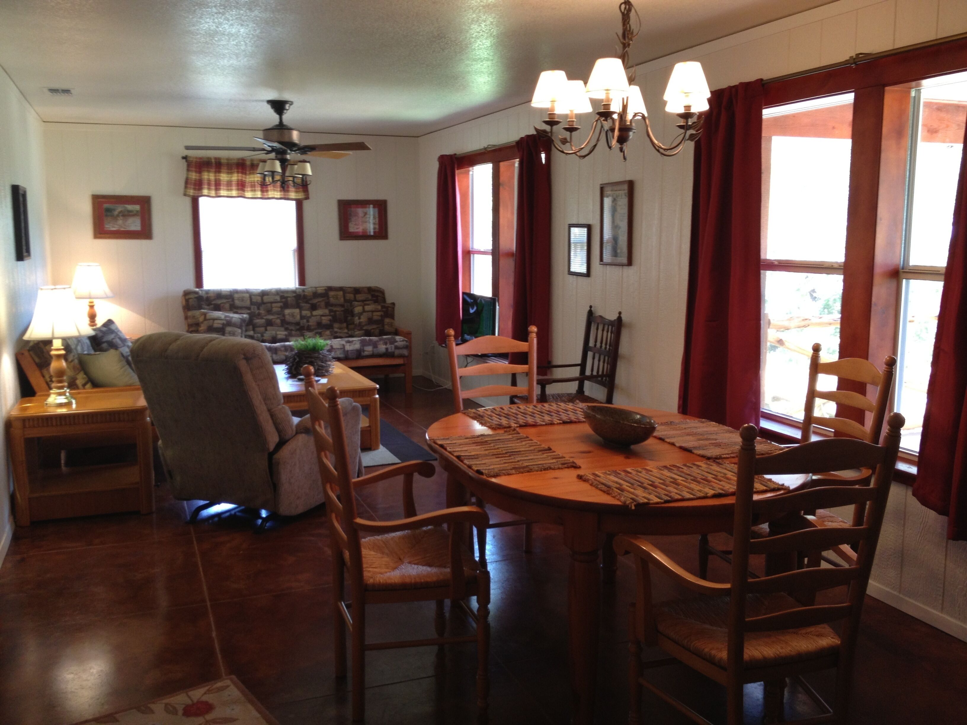A dining area with a round table, chairs, and a chandelier. There is a sofa and a chair in the background.