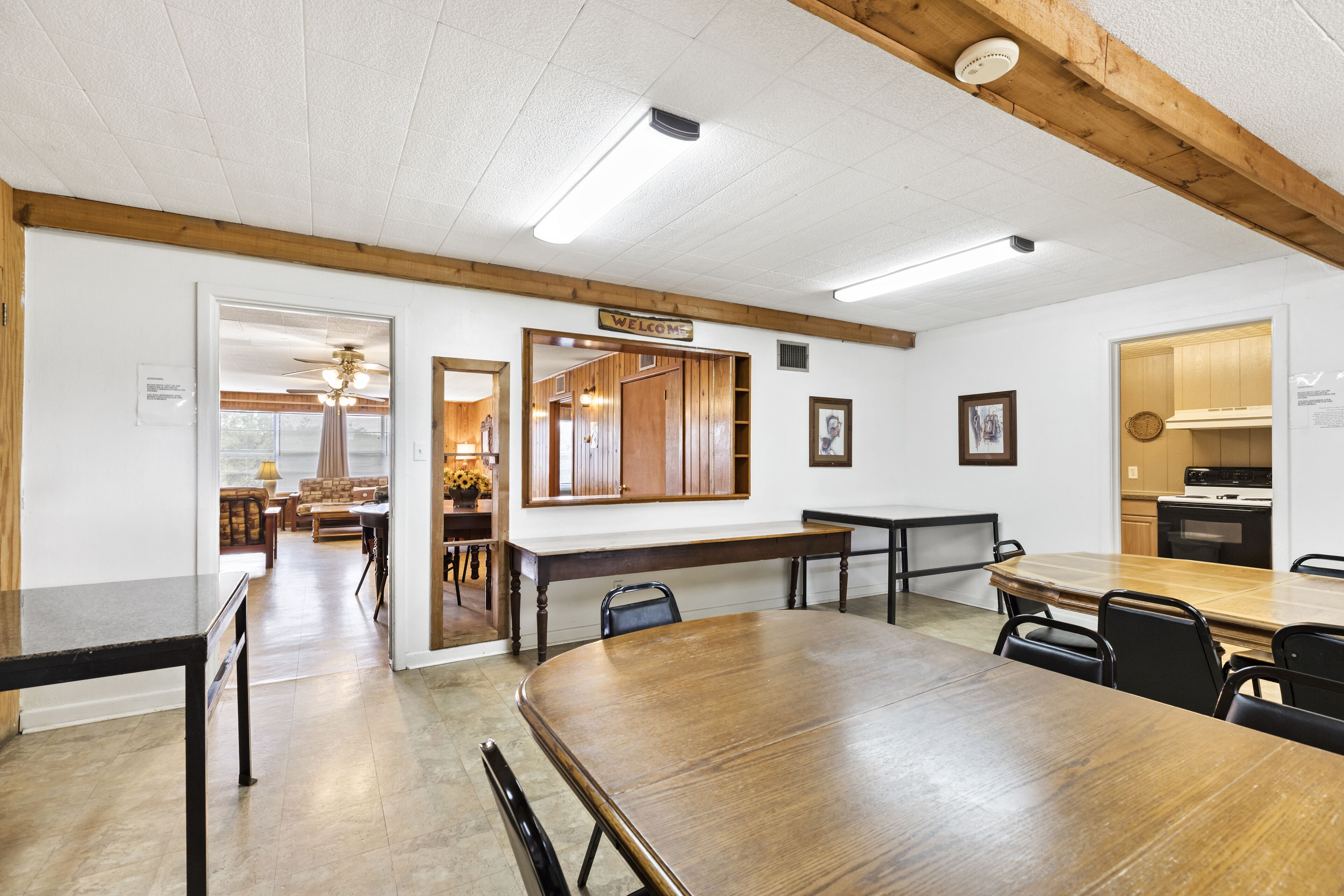A spacious dining area with a large wooden table, several chairs, and a "Welcome" sign.