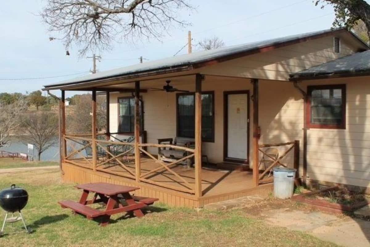 Ein eingeschossiges Haus mit einer überdachten Veranda, einem Grill und einem Picknicktisch.