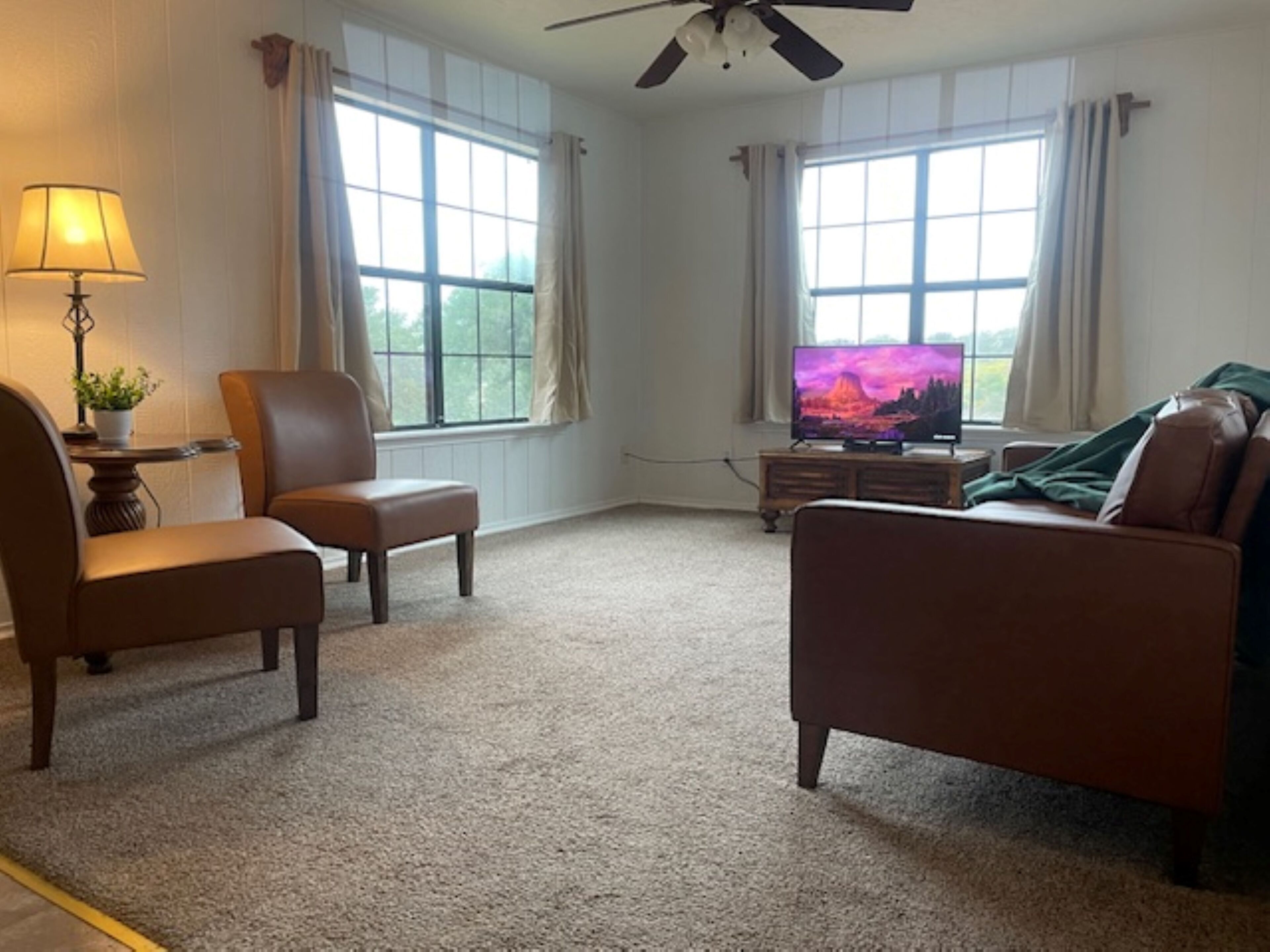Ein Wohnzimmer mit einer Couch, einem Sessel, einem Fernseher und einem Deckenventilator.