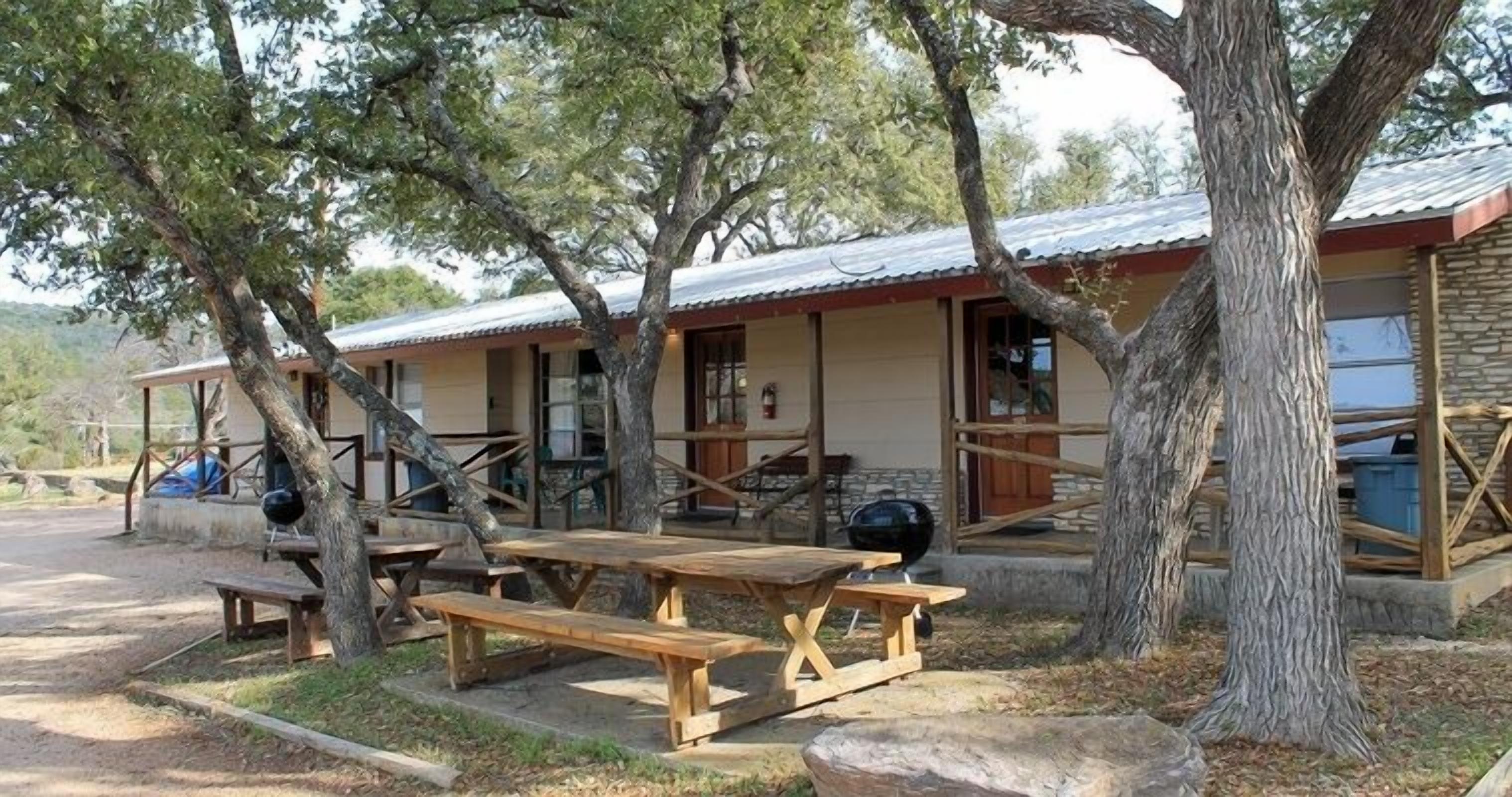 A rustic cabin with a covered porch, picnic tables, and a barbecue grill.