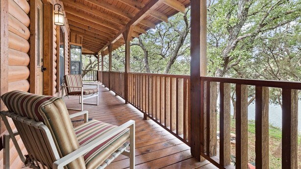 Una cabaña de madera con porche cubierto, una silla y vistas a árboles y agua.