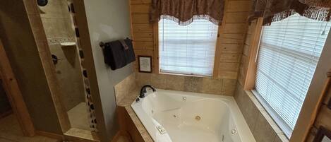 A bathroom with a bathtub, a shower, and a window with blinds.