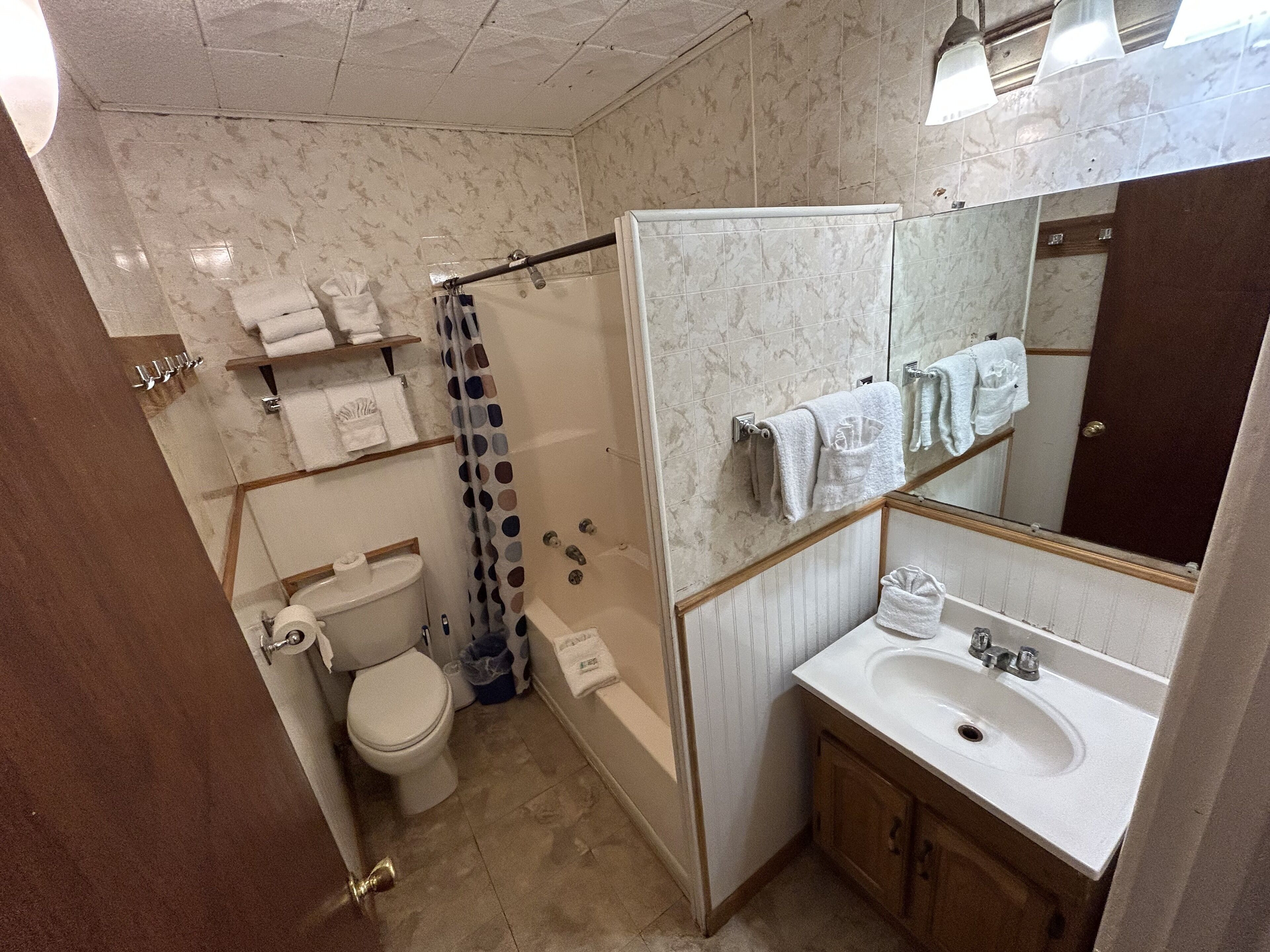 A bathroom with a toilet, sink, and shower. There are shelves with towels and a mirror above the sink.