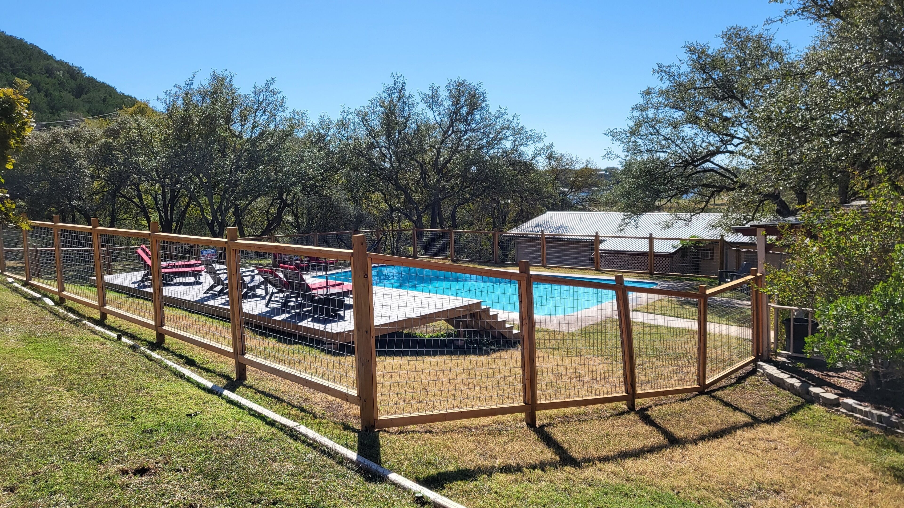 A fenced backyard with a swimming pool, lounge chairs, and a small building.