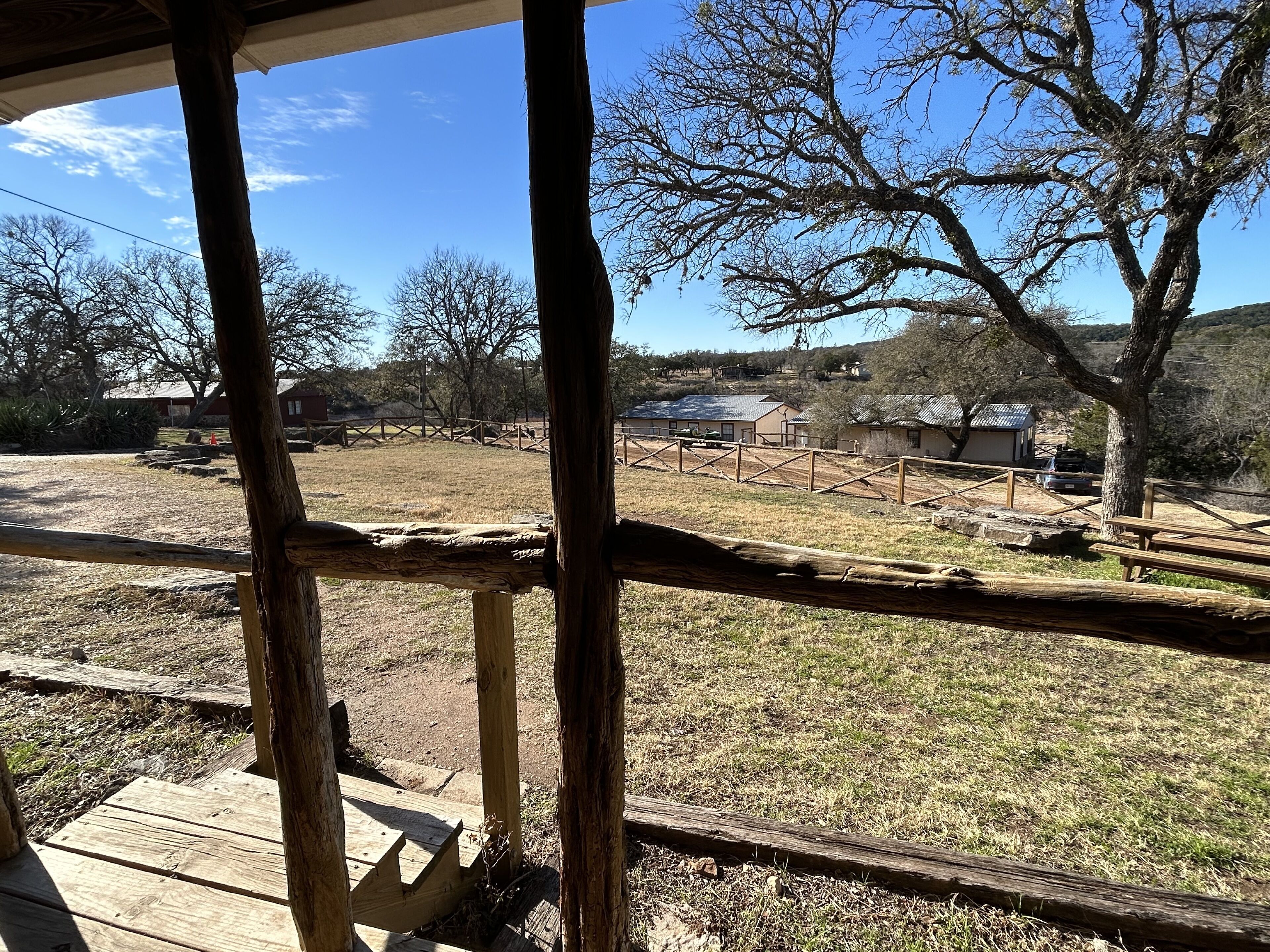 A wooden deck with a view of a fenced outdoor area, including a building and trees.