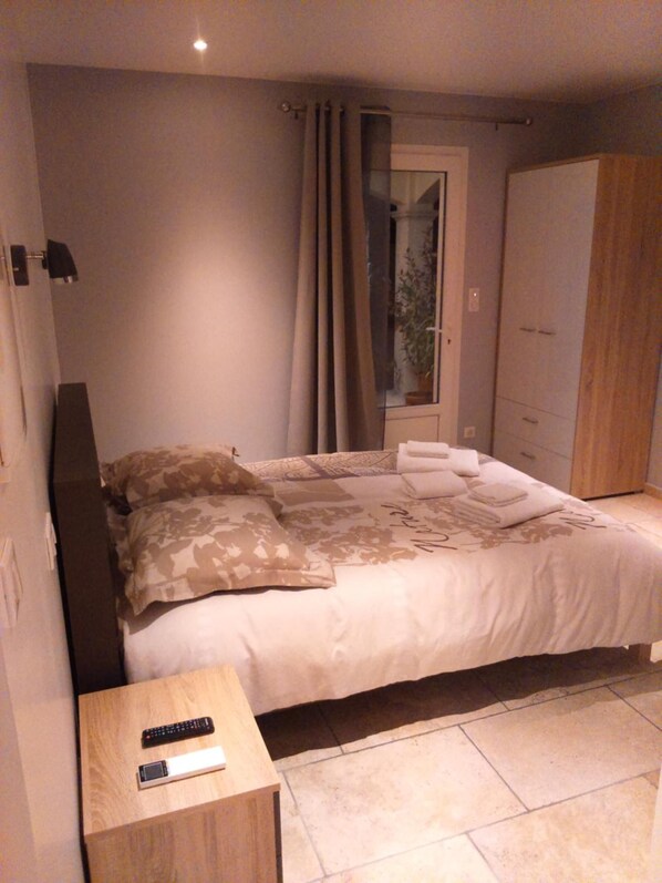 Un dormitorio con cama, mesita de noche, armario y ventana con cortinas.