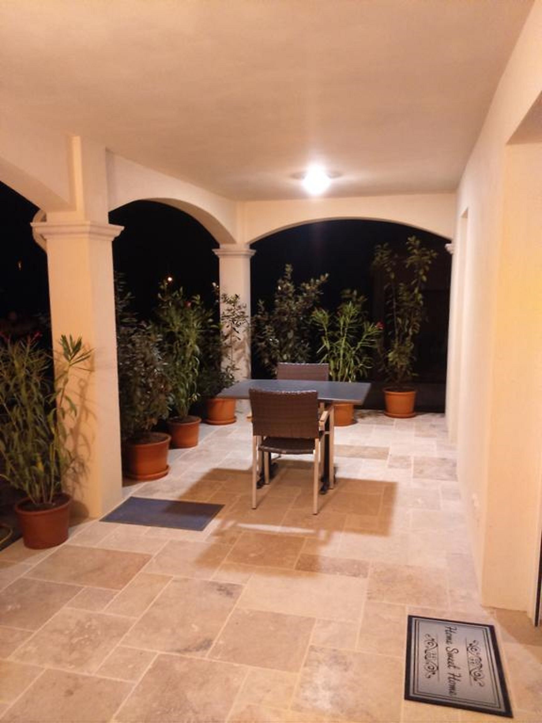 Un patio al aire libre con mesa y sillas, rodeado de plantas en macetas y un piso de baldosas.