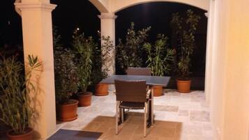 Un patio al aire libre con mesa y sillas, rodeado de plantas en macetas y un piso de baldosas.