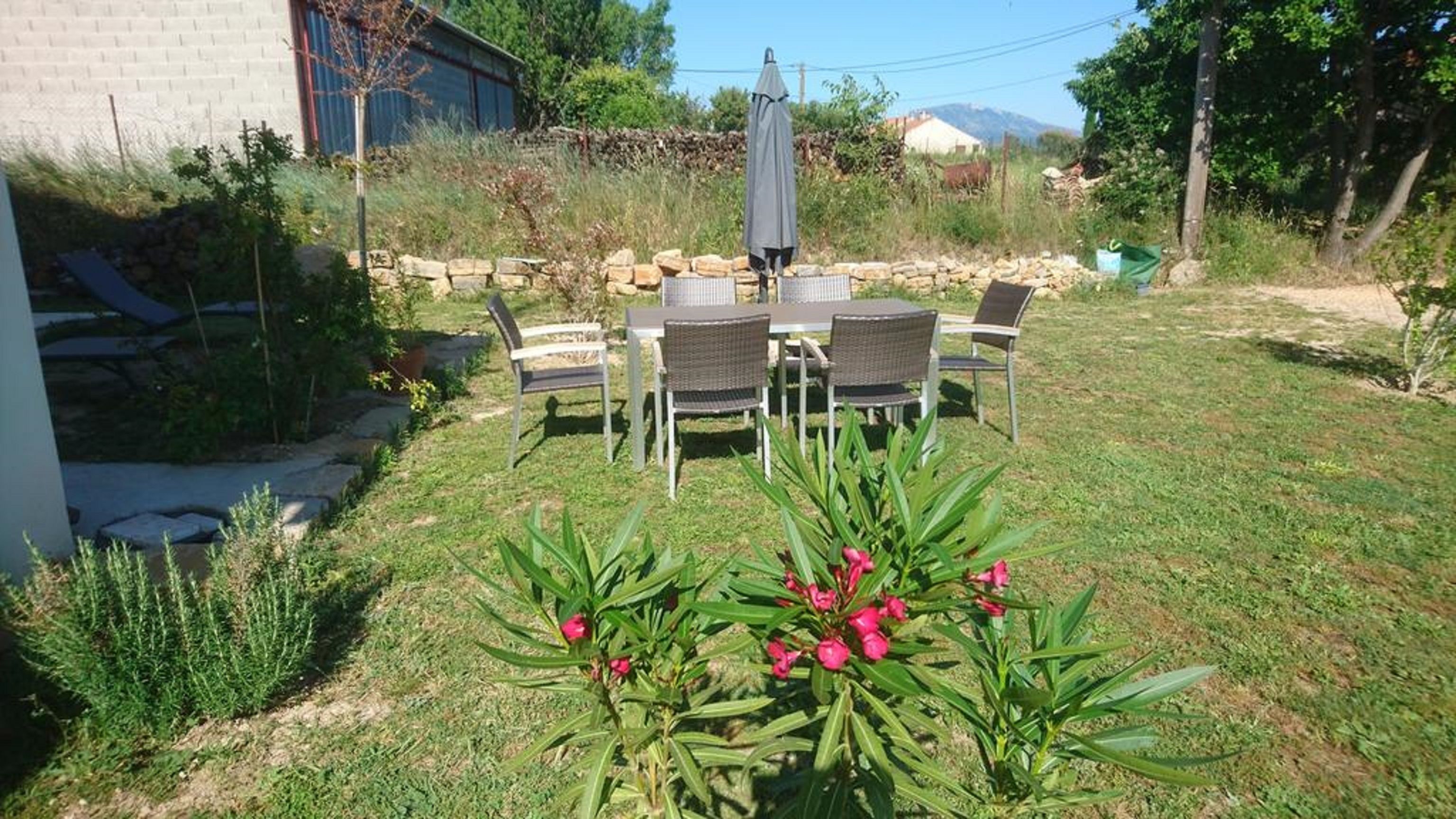 Une terrasse avec une table et des chaises, entourée d’un jardin agrémenté de plantes et d’un mur en pierre.