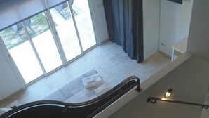 A room with a bed, a window with curtains, a desk with a lamp, and a staircase.