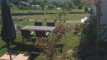 Eine Terrasse im Freien mit Tisch und Stühlen, umgeben von Grünpflanzen und blauem Himmel.