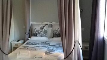 A bedroom with a bed, curtains, a nightstand, and a wall-mounted lamp.