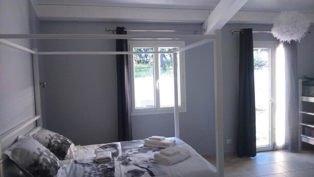 A bedroom with a four-poster bed, a window with curtains, and a chandelier.
