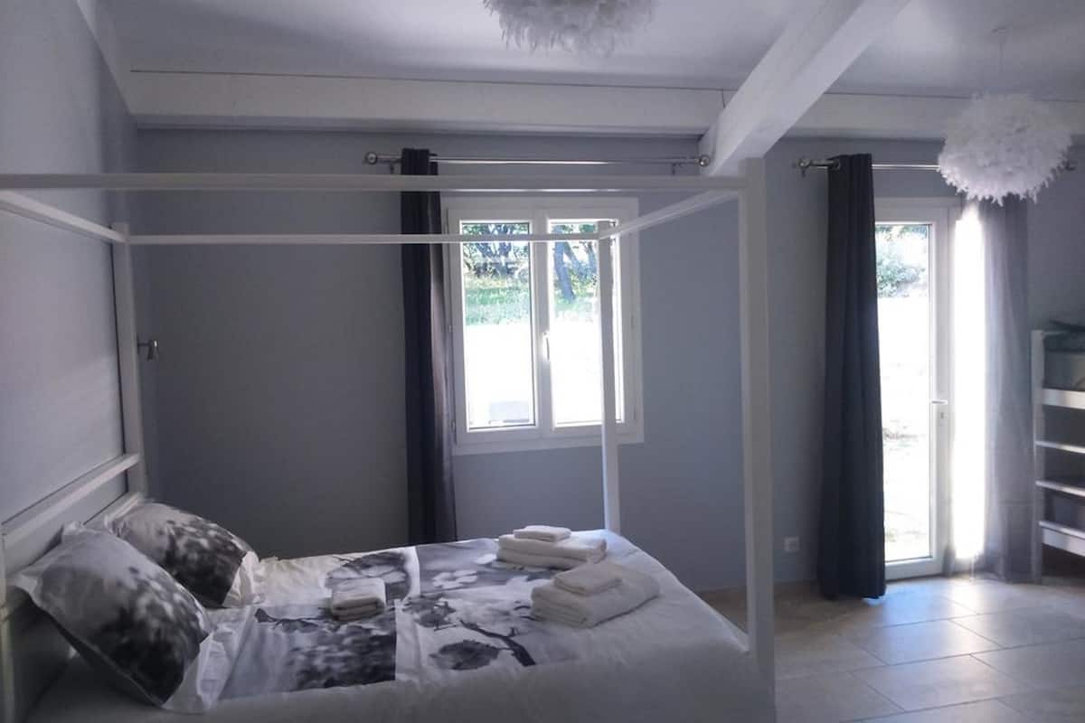 Een slaapkamer met een hemelbed, een raam met gordijnen en een kroonluchter.