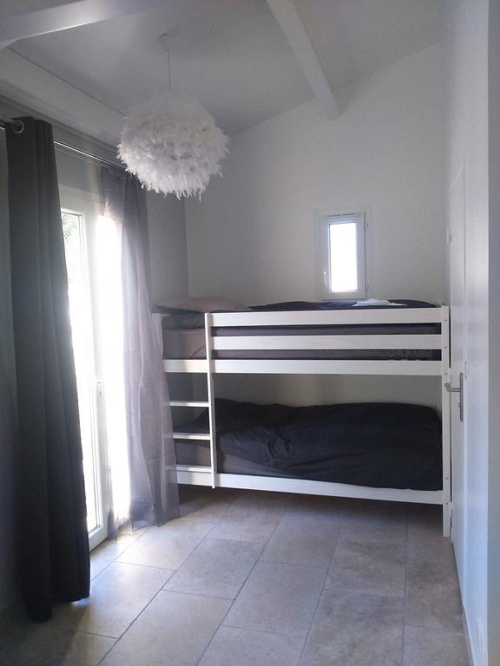 A bunk bed room with a window, curtains, and a fluffy white hanging light fixture.