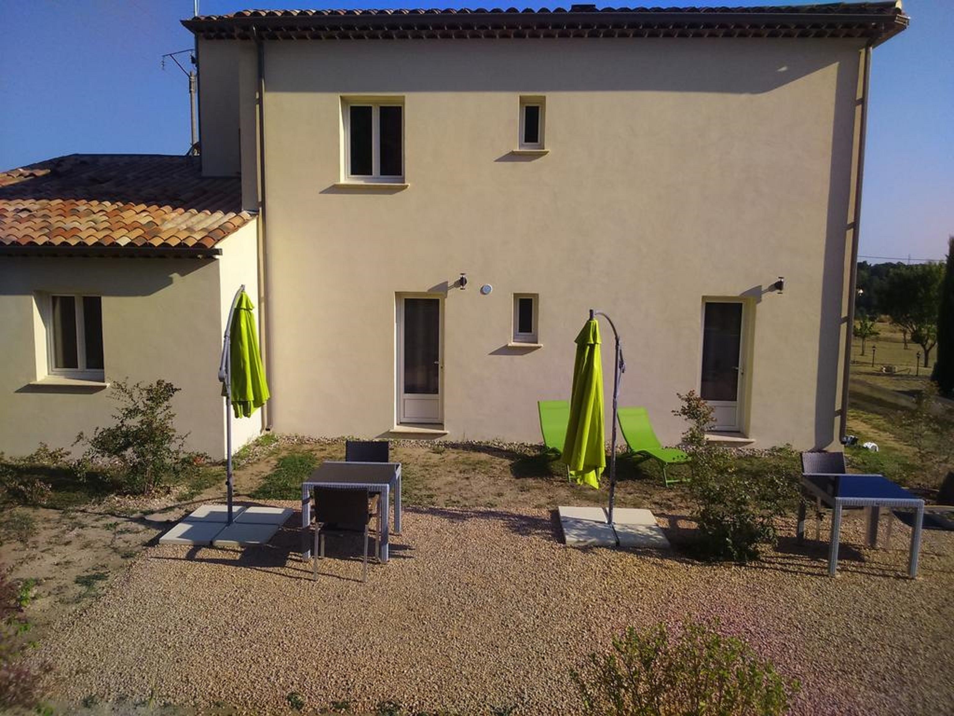 A two-story building with a beige exterior, a tiled roof, and a gravel patio with outdoor furniture and umbrellas.