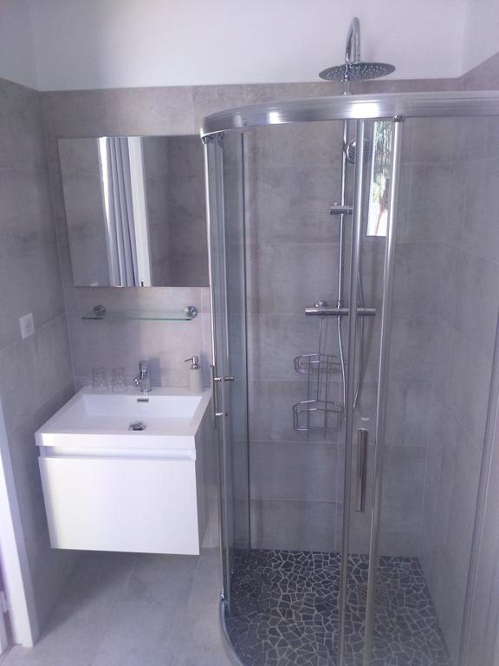 A modern bathroom with a glass-enclosed shower, a white sink, and a mirror above it.