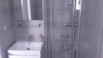 A modern bathroom with a glass-enclosed shower, a white sink, and a mirror above it.