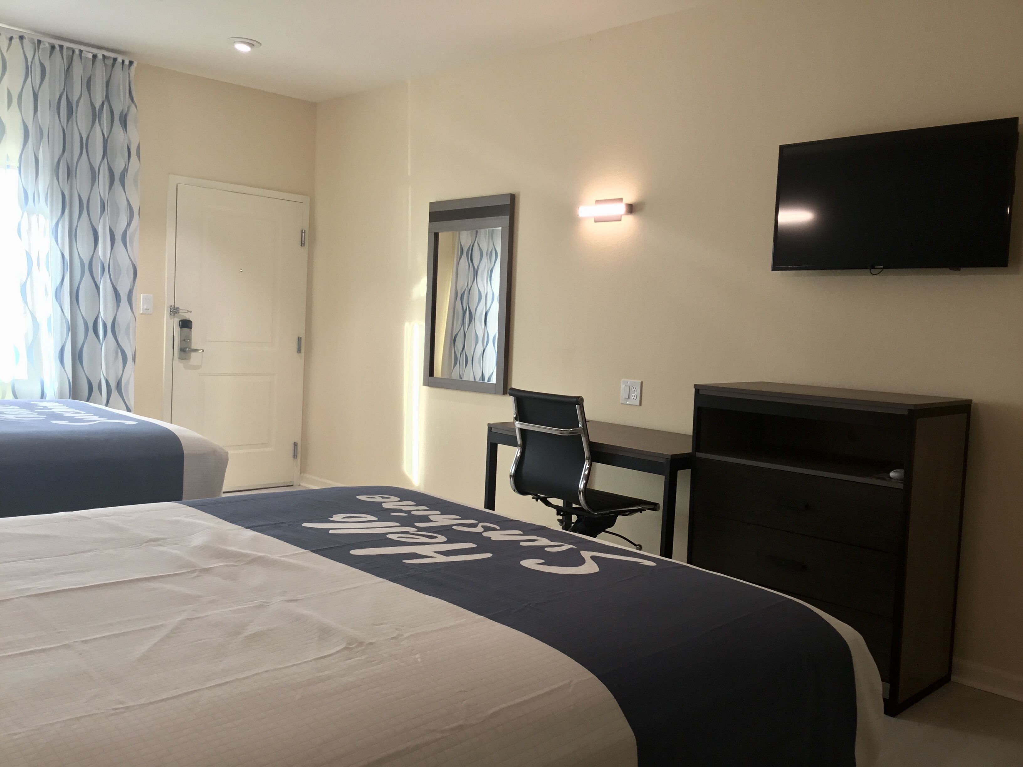 A hotel room with two beds, a desk, a chair, a television, and a wardrobe.