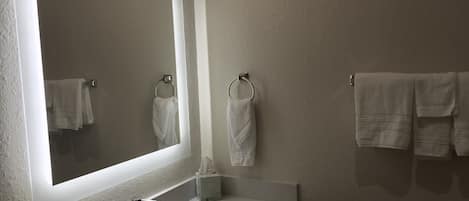 Une salle de bain avec un grand miroir, un lavabo et deux porte-serviettes avec des serviettes.