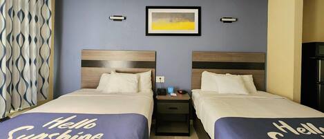 Una habitación de hotel con dos camas, una mesita de noche con un teléfono y una lámpara, un cuadro en la pared y una cortina con un estampado ondulado.