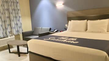 Quarto de hotel com cama grande, mesa de cabeceira, cadeira, escrivaninha e telefone fixado na parede.
