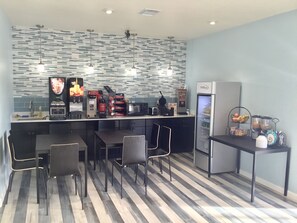 A modern kitchen with a striped tile backsplash, a coffee machine, a microwave, and a refrigerator. There are black chairs and a small table. - Days Inn by Wyndham Freeport (Freeport)