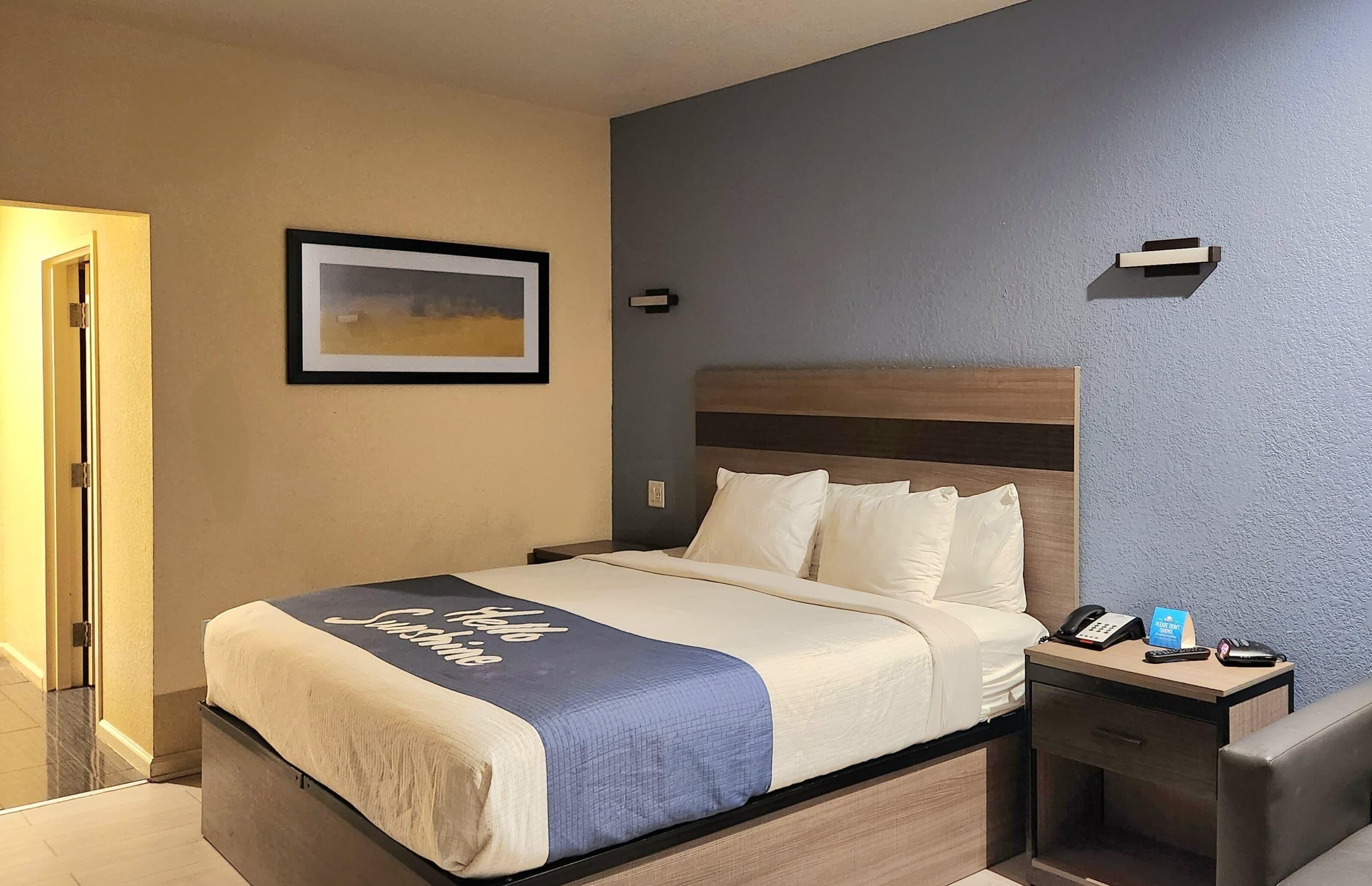 Una habitación de hotel con cama, mesita de noche y un cuadro en la pared.