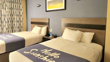 A hotel room with two beds, each with a headboard and a pillow. There is a framed picture on the wall, a curtain with a wavy pattern, and a bedside table with a phone and a small lamp.