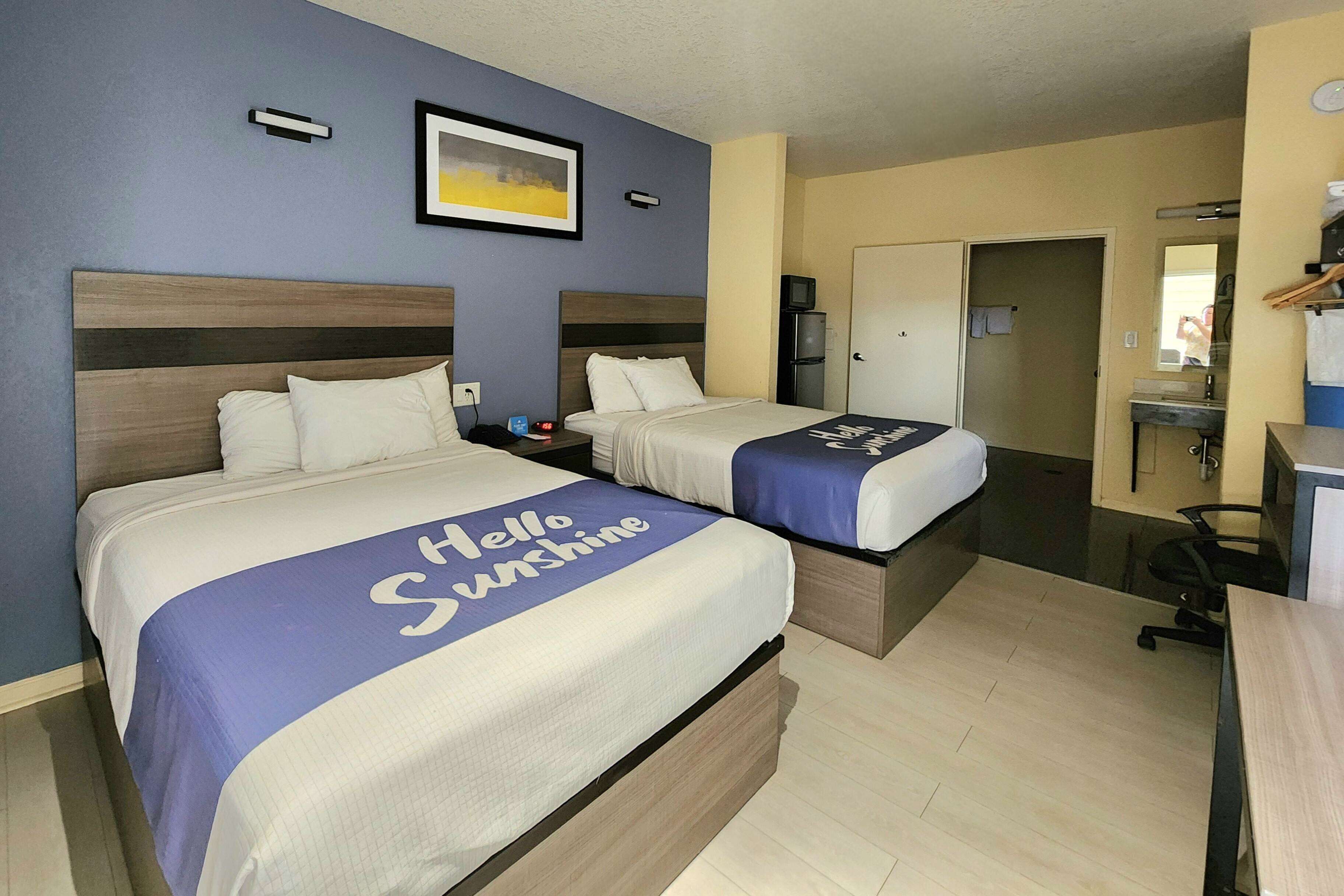 A hotel room with two beds, a desk, a chair, a mirror, and a door.
