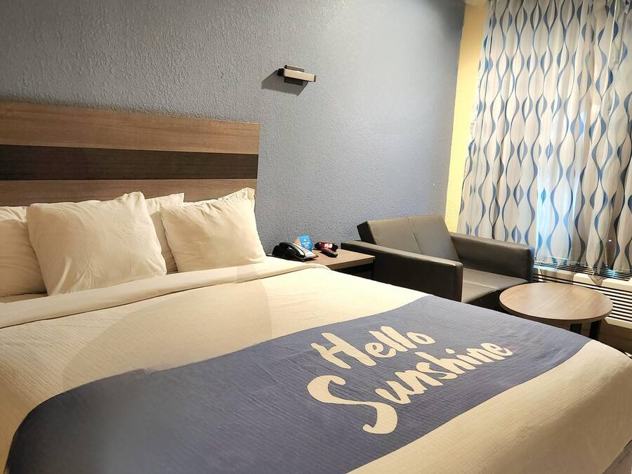 A hotel room with a bed, a desk, a chair, a small table, and a window with patterned curtains.
