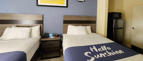 Una habitación de hotel con dos camas, una mesita de noche, un cuadro enmarcado en la pared, un microondas y un refrigerador.