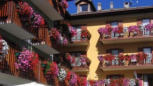 Un hotel de varios pisos con balcones decorados con flores de colores, mobiliario exterior con sombrillas y un cielo azul despejado.